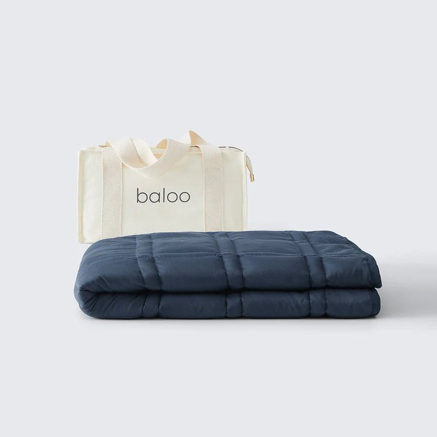 Navy blue weighted blanket with a white tote bag featuring 'baloo' branding on a light gray background.