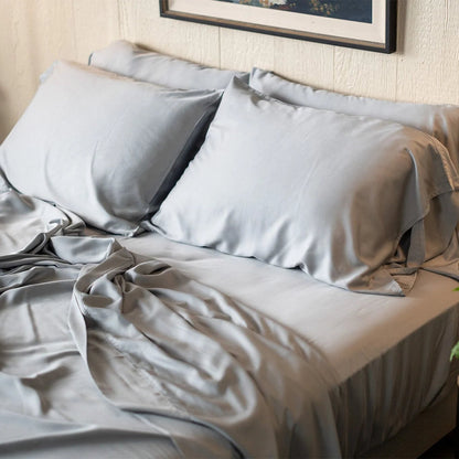 Bed with light gray bedding and pillows in a room setting.