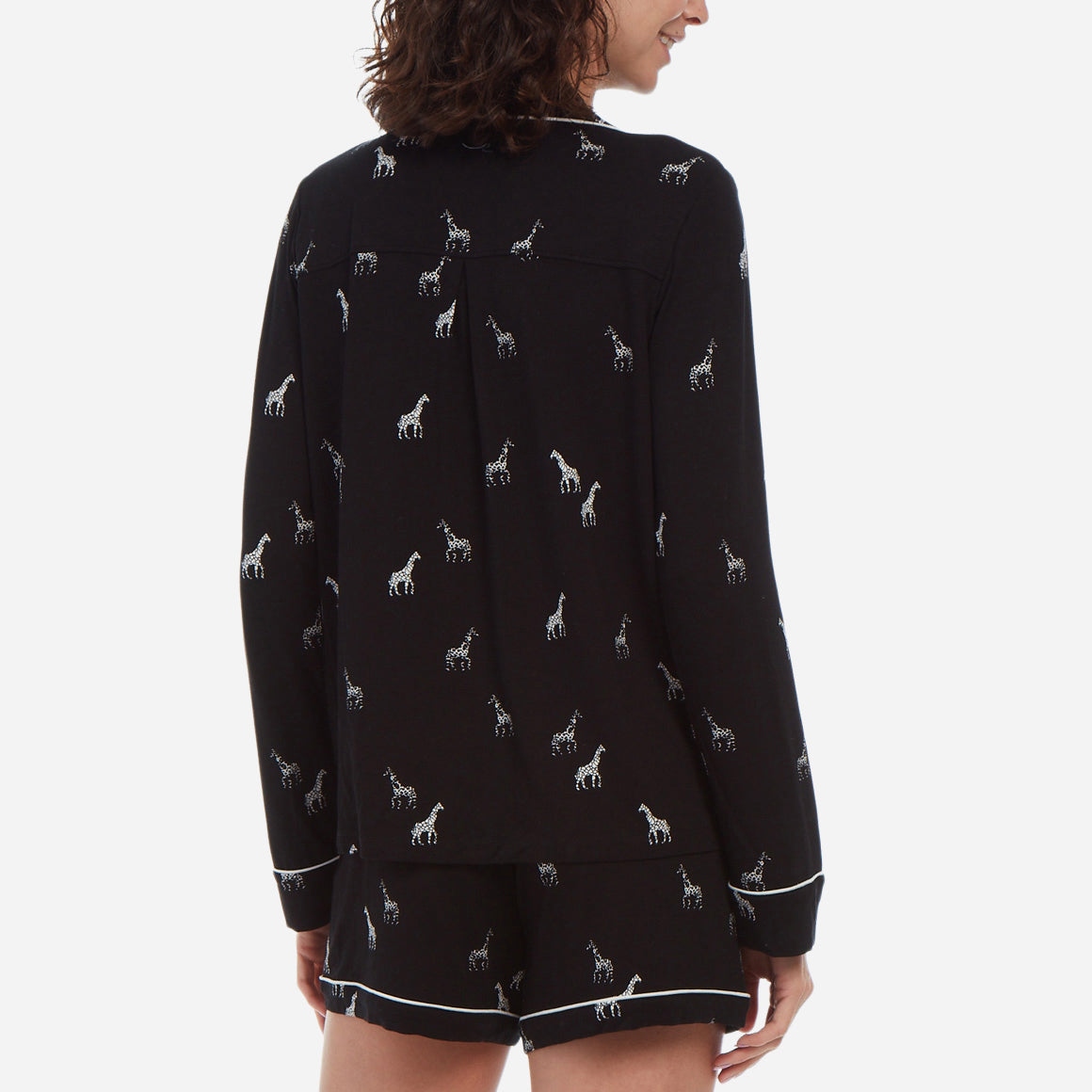 Back-facing female model is wearing a black long sleeve with shorts pj set. The set has a black and white giraffe print.