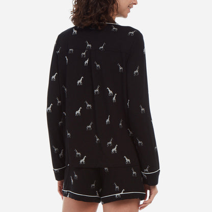 Back-facing female model is wearing a black long sleeve with shorts pj set. The set has a black and white giraffe print.