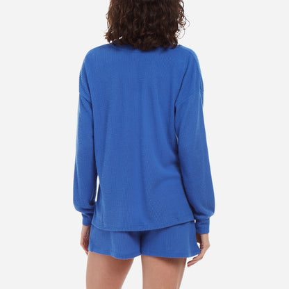 Back-facing female model wearing a long-sleeve top and shorts waffle knit lounge set in royal blue.