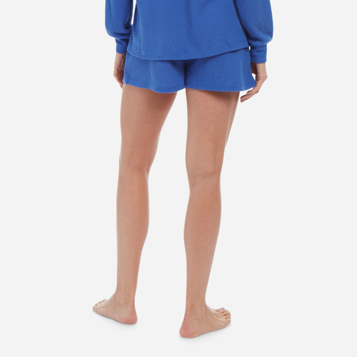 Back-facing female model wearing waffle-knit shorts in royal blue color.