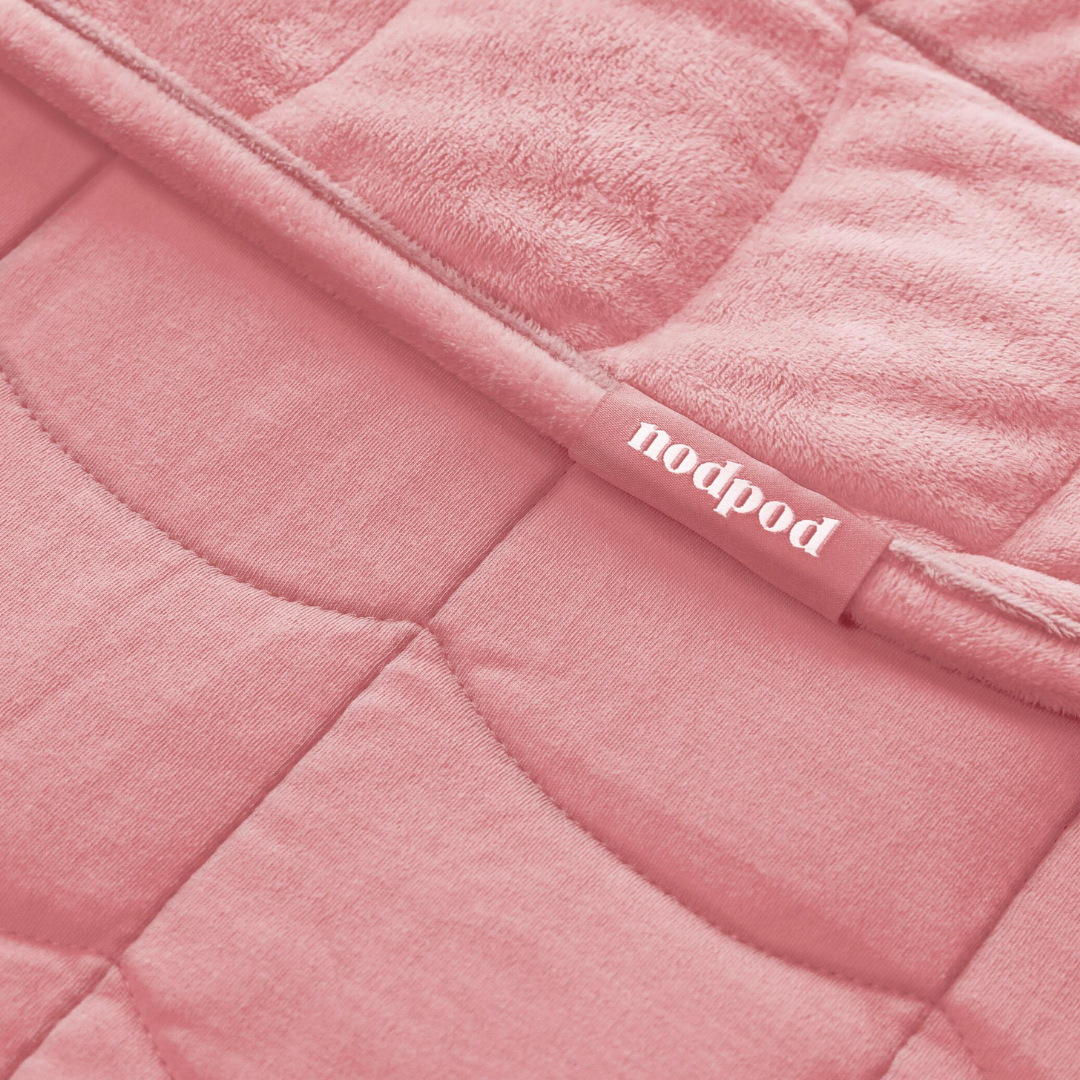 Close-up of a blush pink quilted weighted blanket with 'nodpod' label