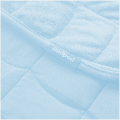 Close-up of a light blue quilted weighted blanket with a 'nodpod' label.