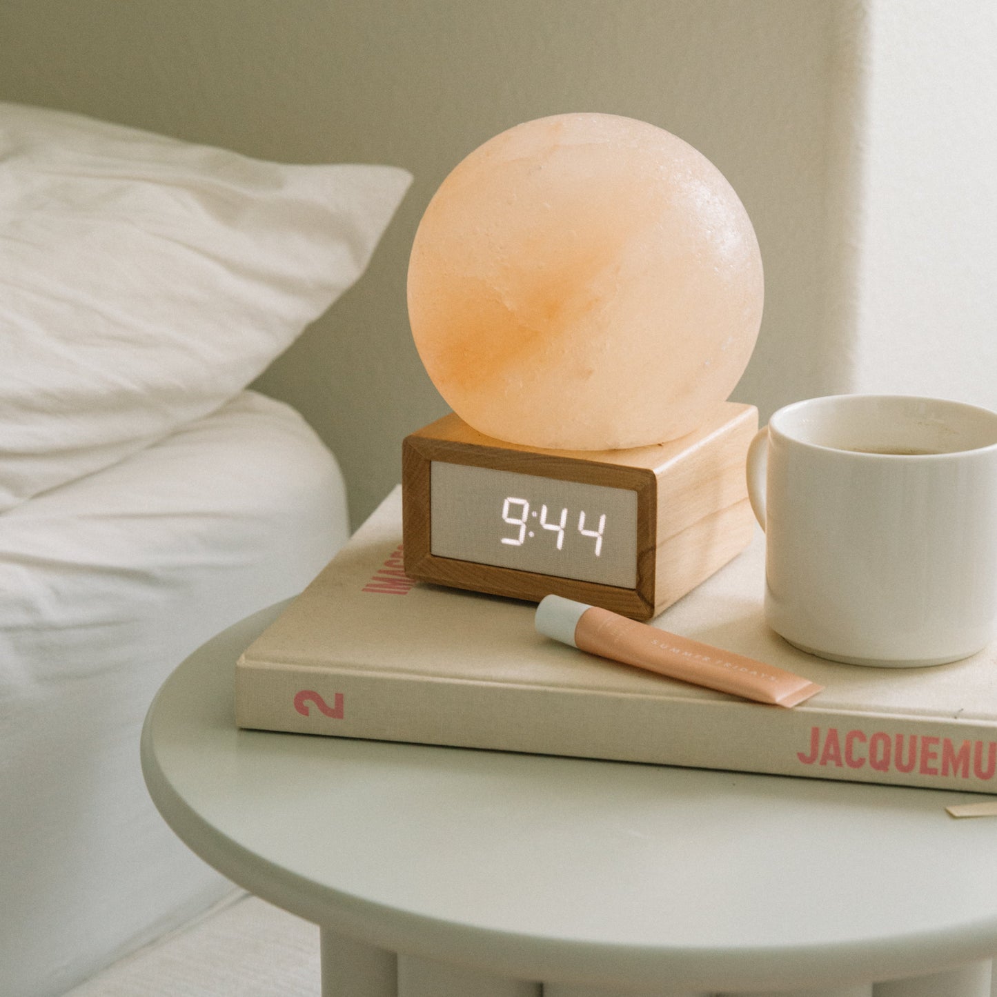 Table with a night light, alarm clock, book, and mug on a neutral background