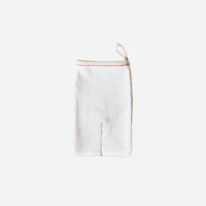 Rectangle shaped body scrub mitt against white background. Cream colored with red piping along opening. A hang tab on top right corner.