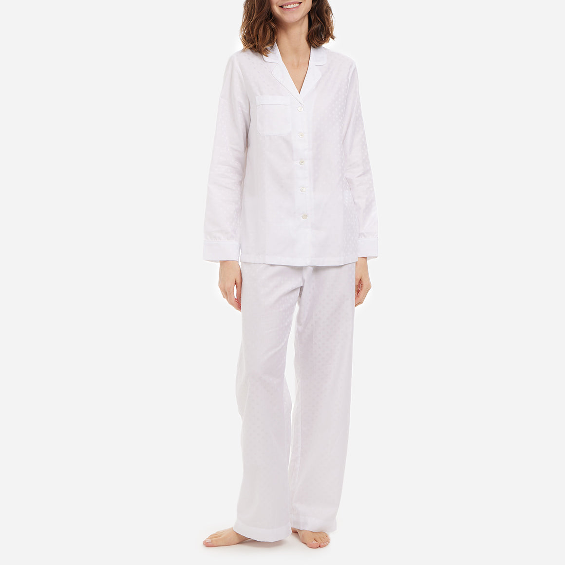 A front-facing model is wearing a long pajama set made of white polka dot cotton jacquard.