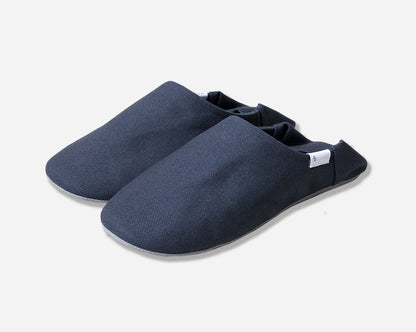 Angled view of navy slippers with heel flap folded down. Shot against a white background. White label with black logo.